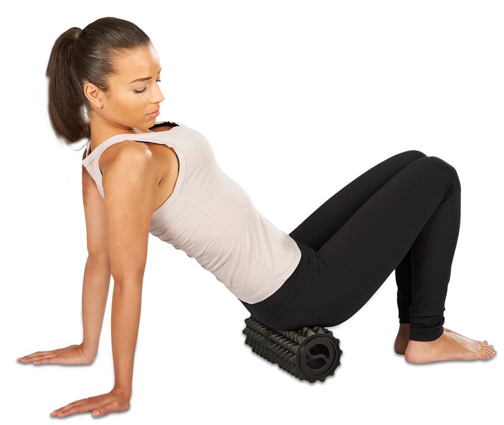 Femme au sol utilisant un rouleau de massage noir sous les fesses.