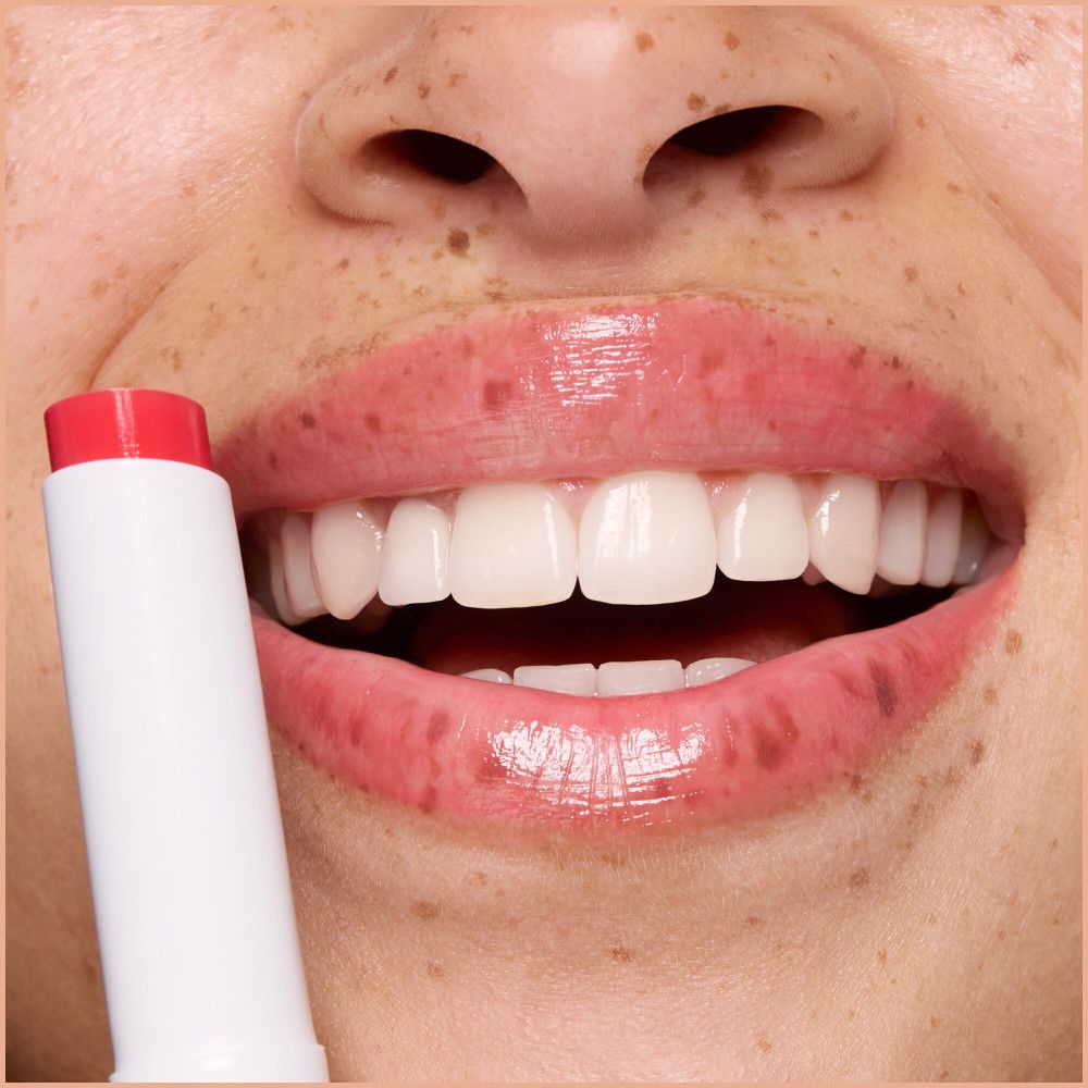 Gros plan sur des lèvres recouvertes de baume à lèvres. Un baume à lèvres est partiellement visible.