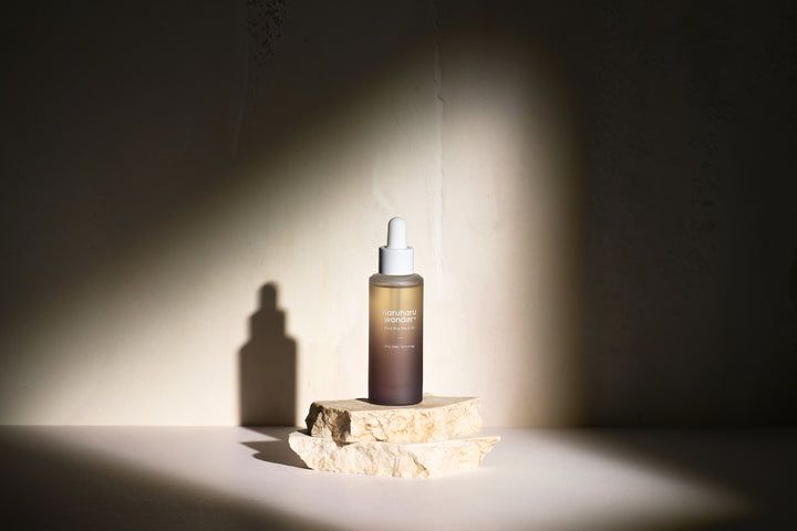 HaruHaru Wonder Black Rice Facial Oil fles op steen. Bruine fles met witte dop, in de schaduw.