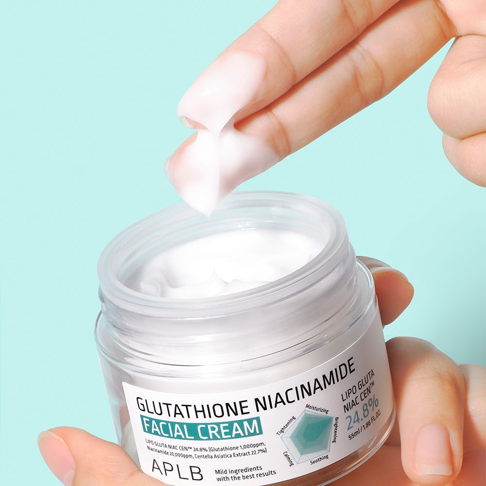 Een hand schept APLB gezichtscrème met glutathion en niacinamide uit een glazen pot.