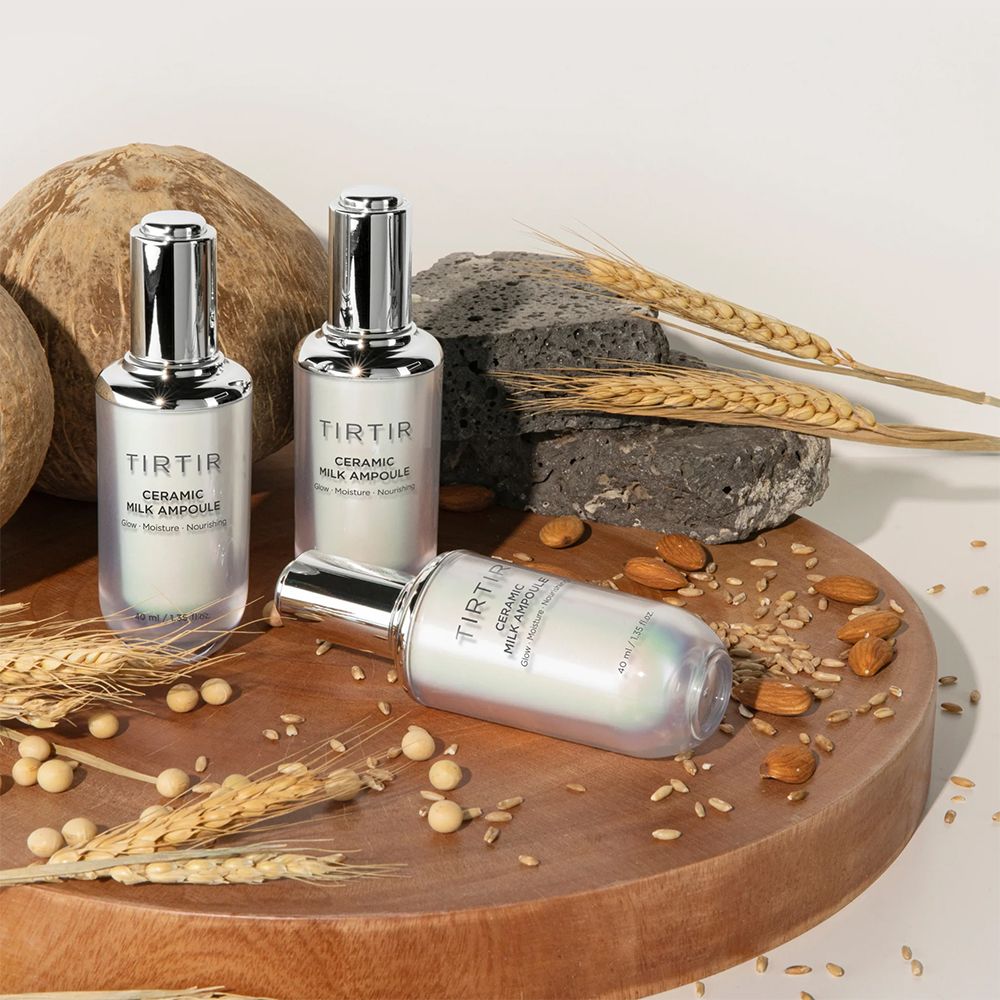 Drie TIRTIR Ceramic Milk Ampullen op houten plank. Tekst: Glow, Moisture, Nourishing. Decoratie: granen, noten, kokos.