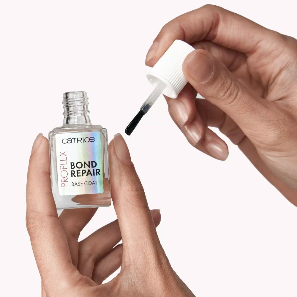 Handen die Catrice Bond Repair Base Coat fles en kwast vasthouden. Naam en merk zichtbaar.