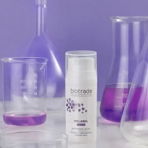 Flacon blanc avec pompe. Inscription: Biotrade, Melabel Forte, Brightening Cream. Verrerie de laboratoire en arrière-plan.