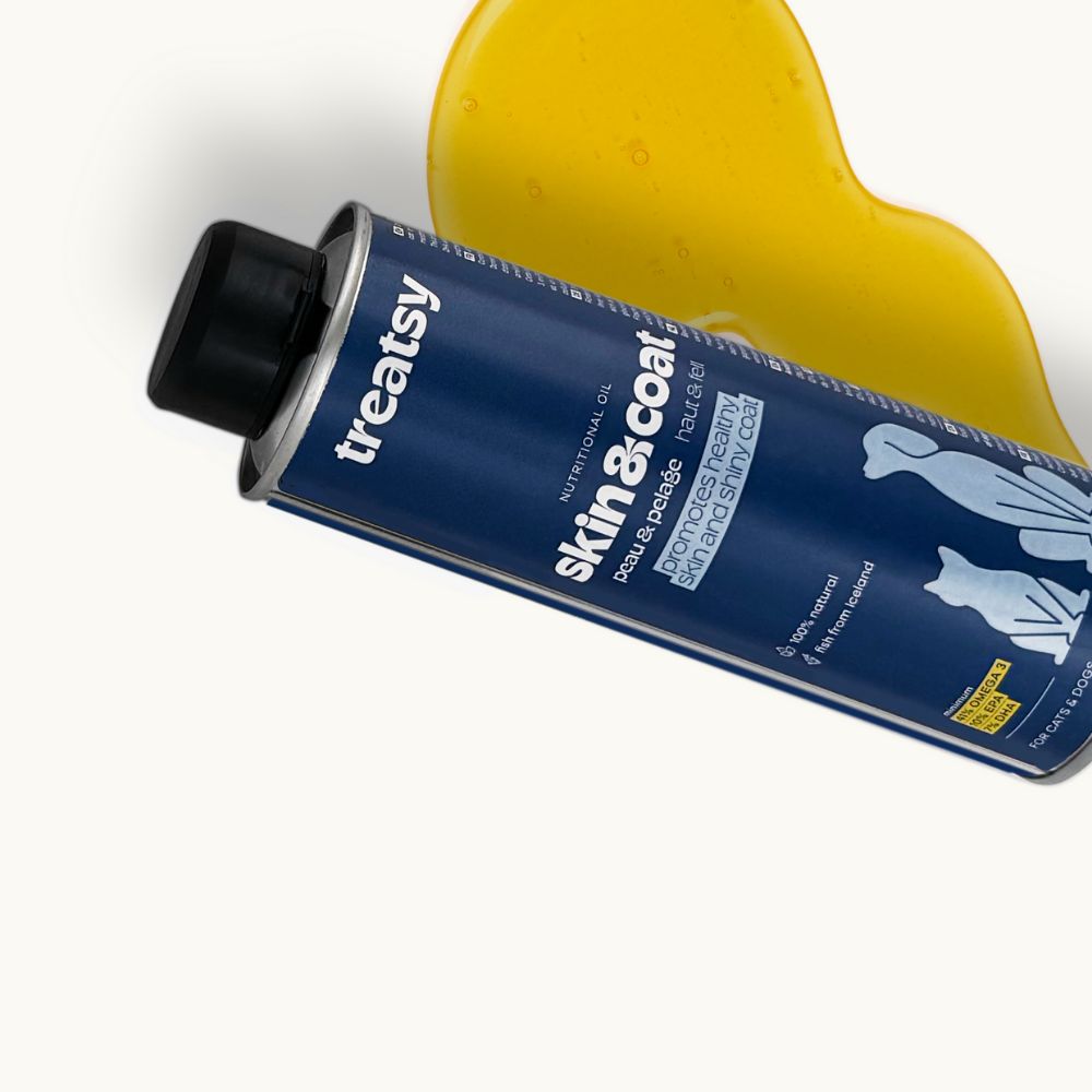 Blauwe bus met zwarte deksel. Opschrift: Treatsy, Skin & Coat. Gele olie ernaast.