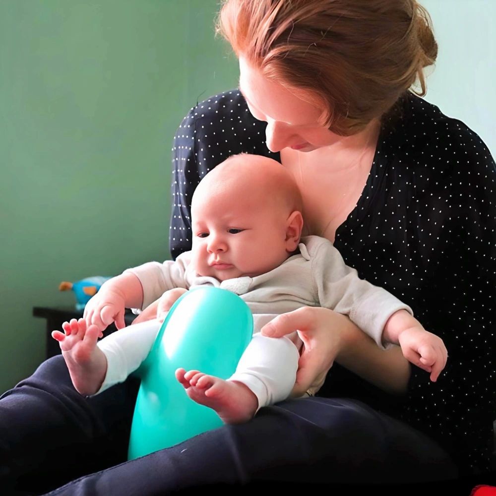Baby zit op een turquoise potje, vastgehouden door een persoon.