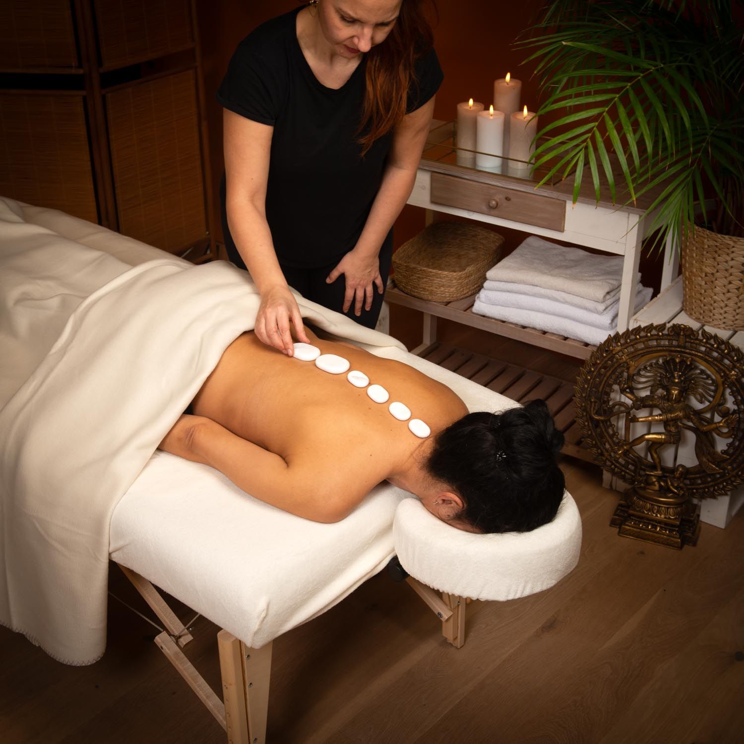 Persoon legt witte, ovale stenen op de rug van een ander. Op een massagetafel.