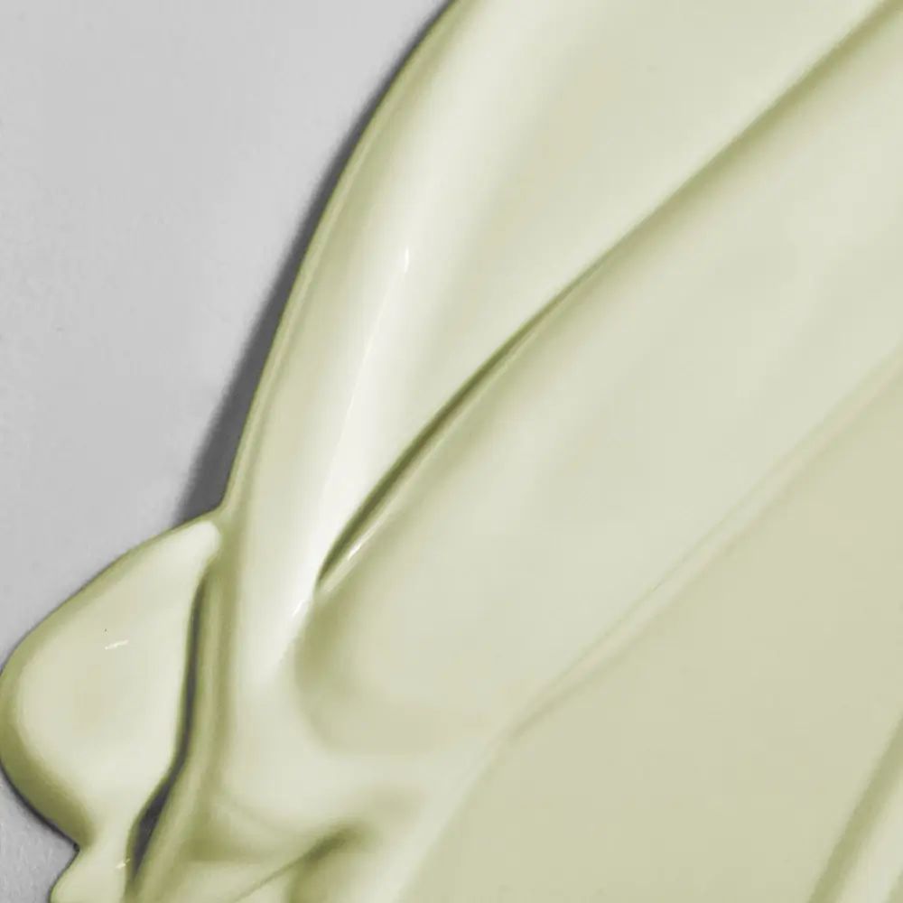 Close-up van een crème-achtige substantie. De textuur is glad en glanzend. De achtergrond is lichtgrijs.