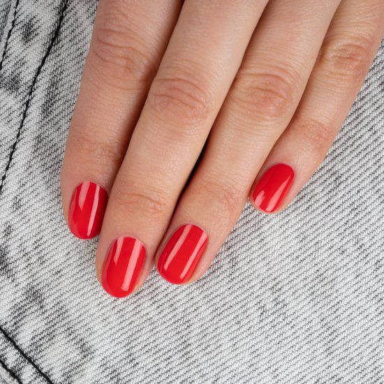 Main avec ongles rouges vernis. Les ongles sont de forme ovale et brillants.
