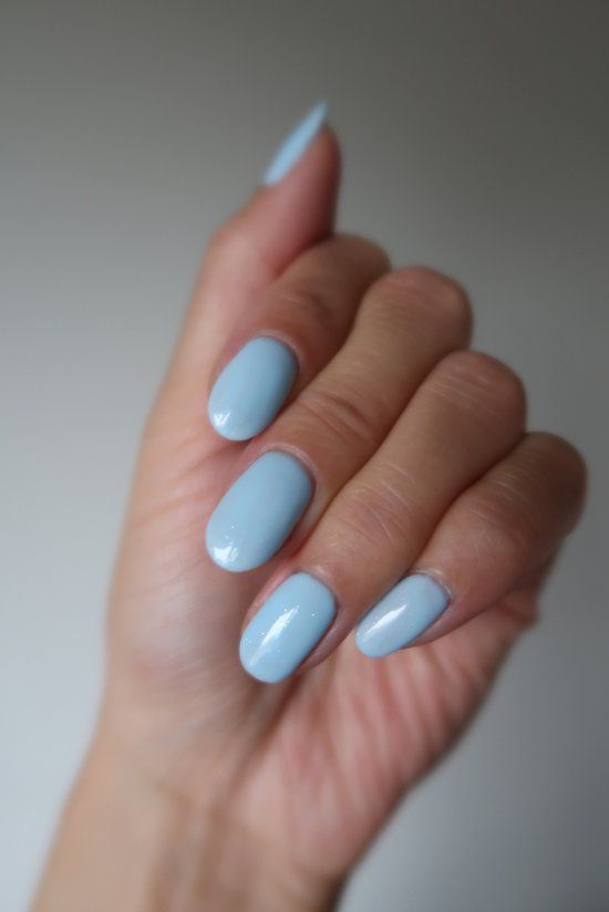 Main avec ongles peints en bleu clair. Cinq ongles à surface lisse. Couleur de peau claire.