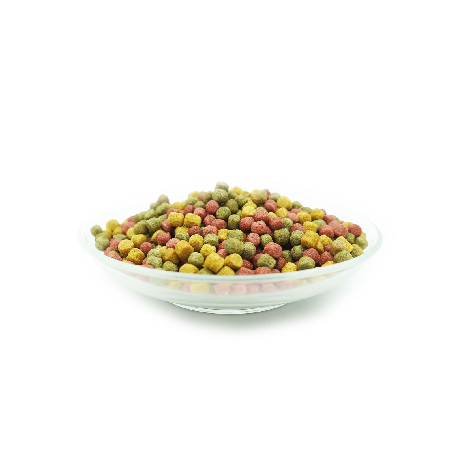Granulés multicolores dans un bol en verre. Les boules sont vertes, rouges et jaunes. Bol transparent sur fond blanc.