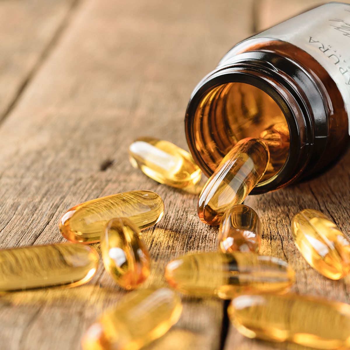 Amberkleurige capsules vallen uit een geopende fles op een houten ondergrond.