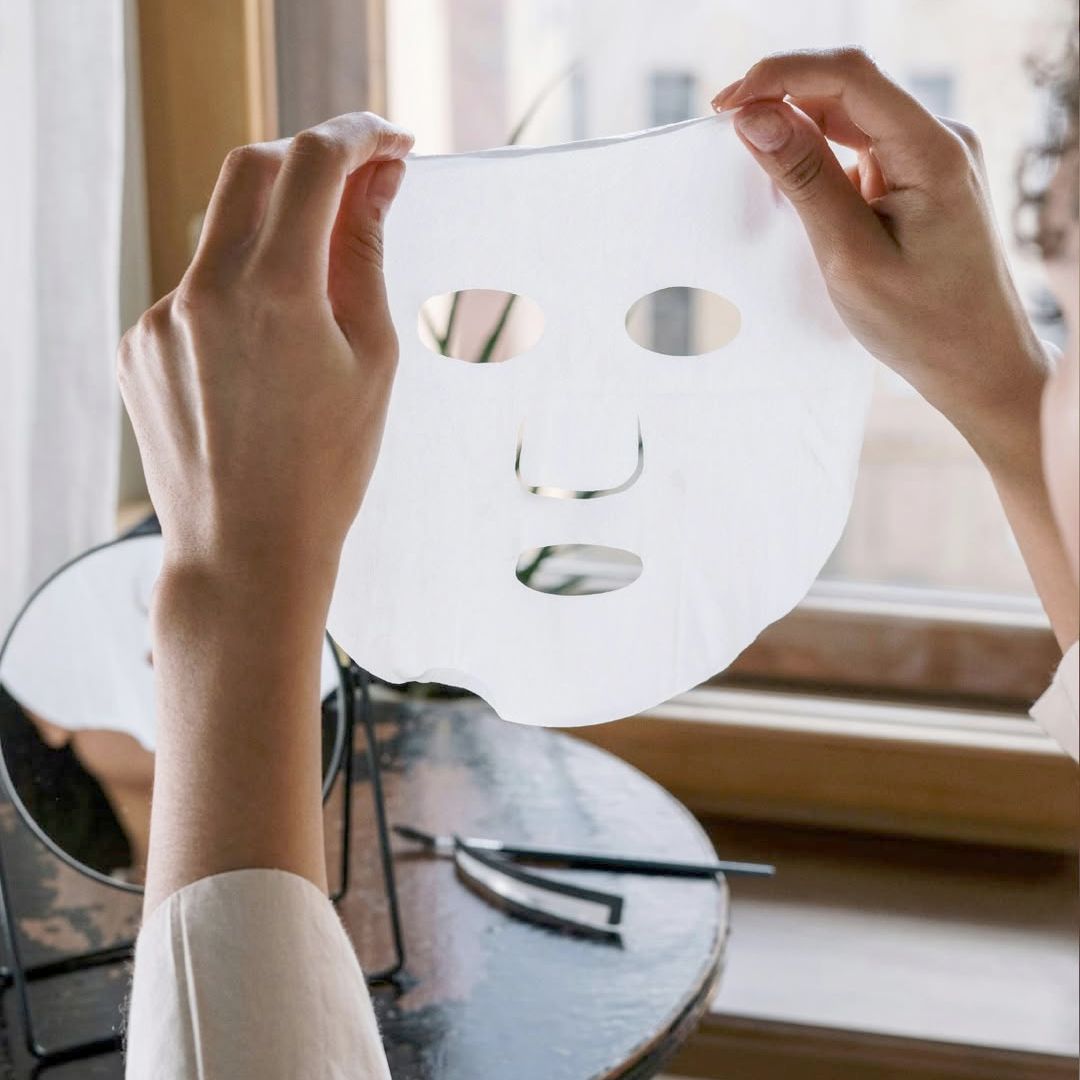 Handen die een wit gezichtsmasker vasthouden met oog- en mondopeningen.