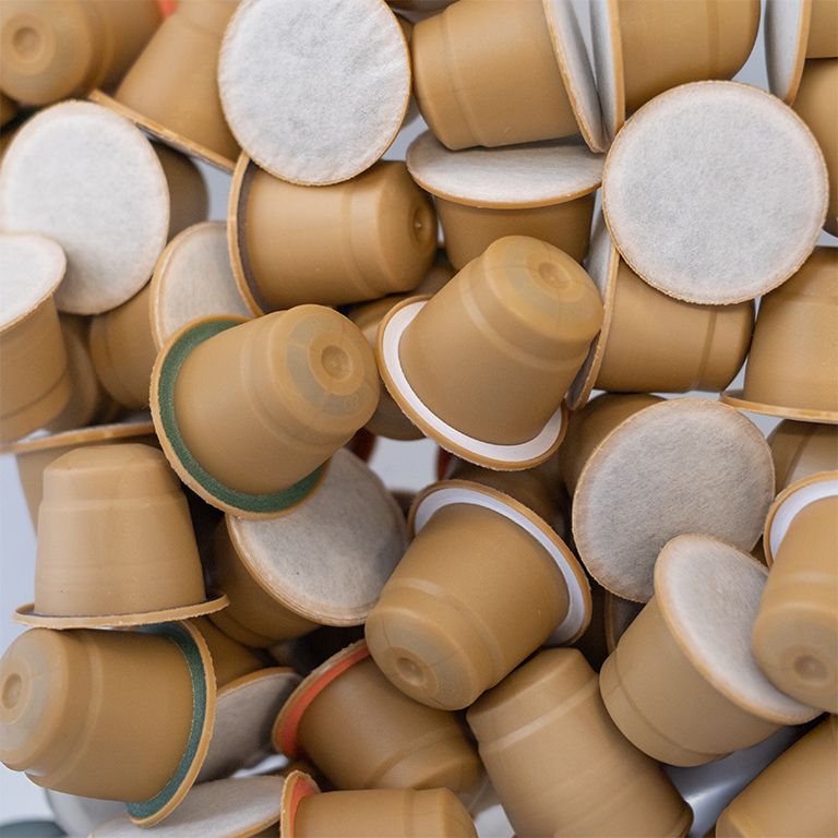 Stapel koffiecapsules. Capsules zijn bruin met wit filter. Sommige capsules zijn open.