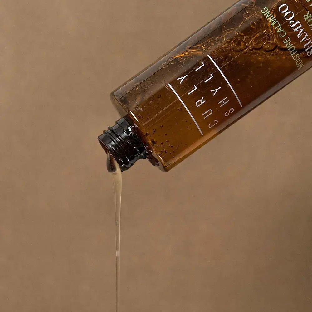 Bouteille marron versant du produit. Inscription: Curly Shyll, Moisture Calming Shampoo.