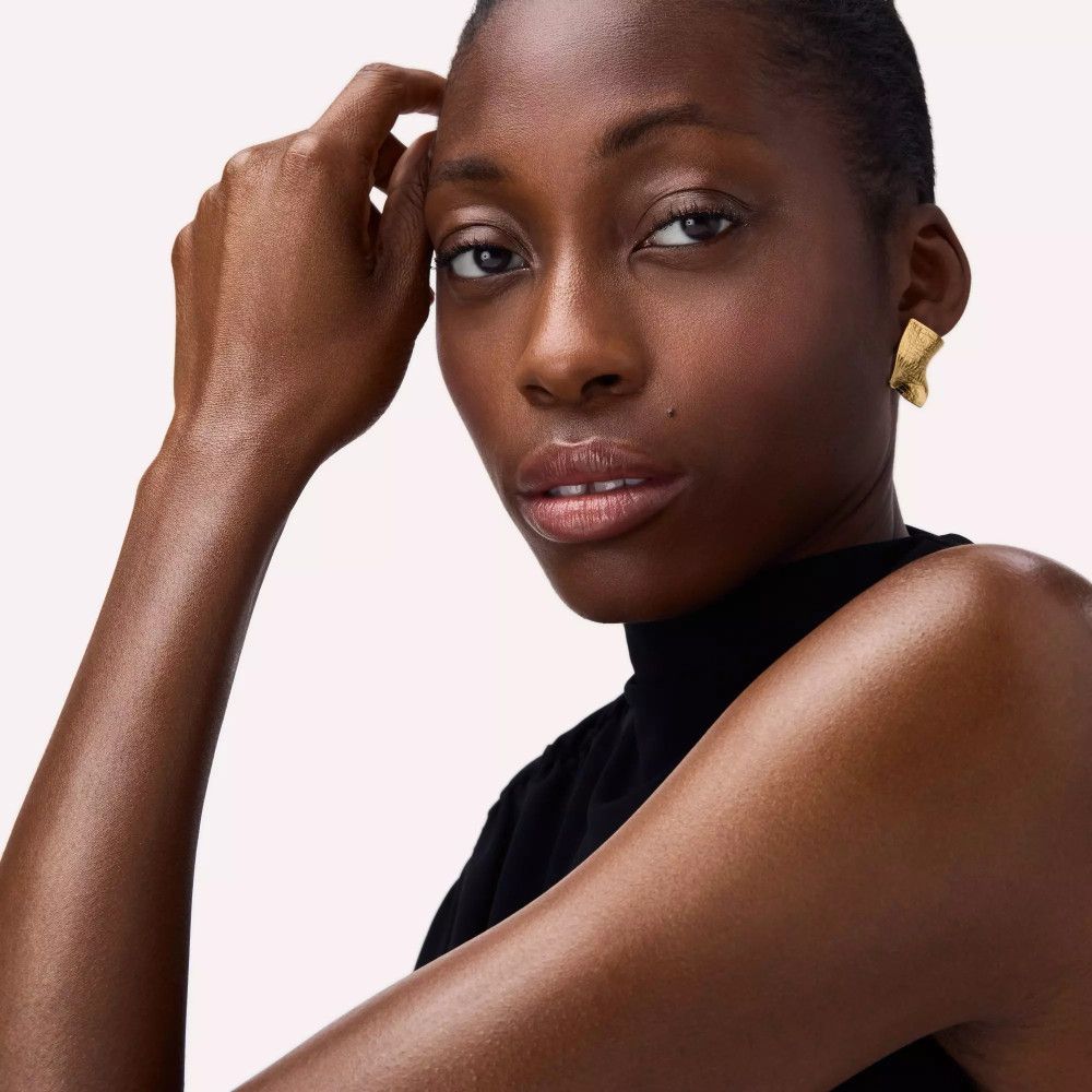 Portrait d'une femme à la peau foncée. Elle porte des boucles d'oreilles dorées et un haut noir.