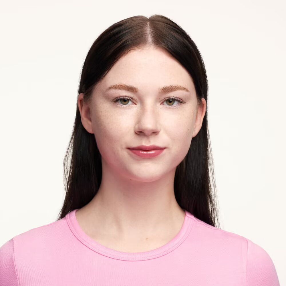 Portrait d'une femme aux longs cheveux foncés et aux lèvres roses. Elle porte un haut rose.