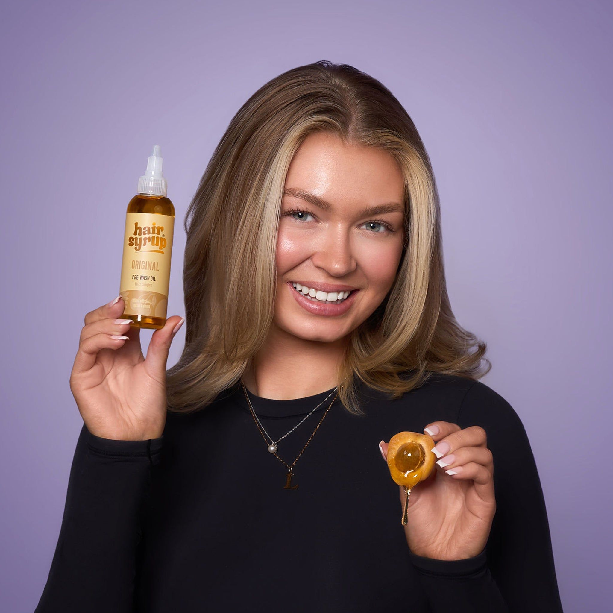 Vrouw houdt een fles Hair Syrup The Original en een vrucht vast. Ze lacht in de camera.