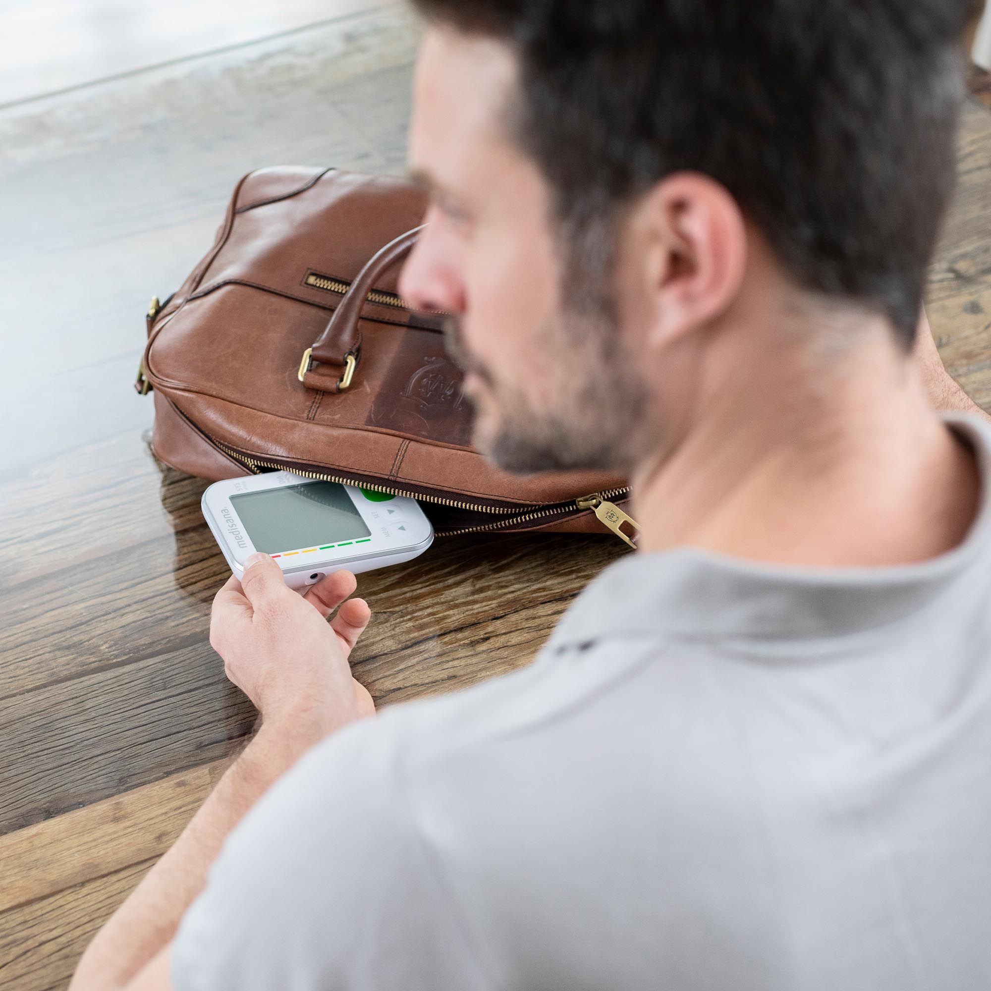 Man legt bloeddrukmeter in een tas. Apparaat en tas op houten oppervlak.