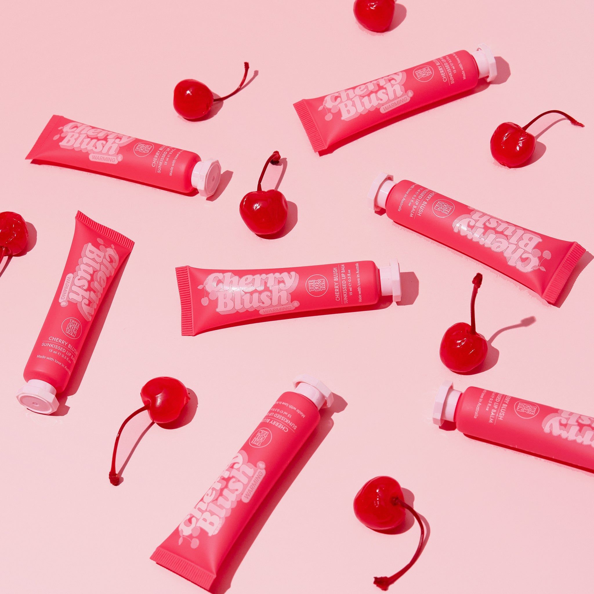 Plusieurs tubes 'Cherry Blush' et cerises sur fond rose. Nom du produit et marque visibles.