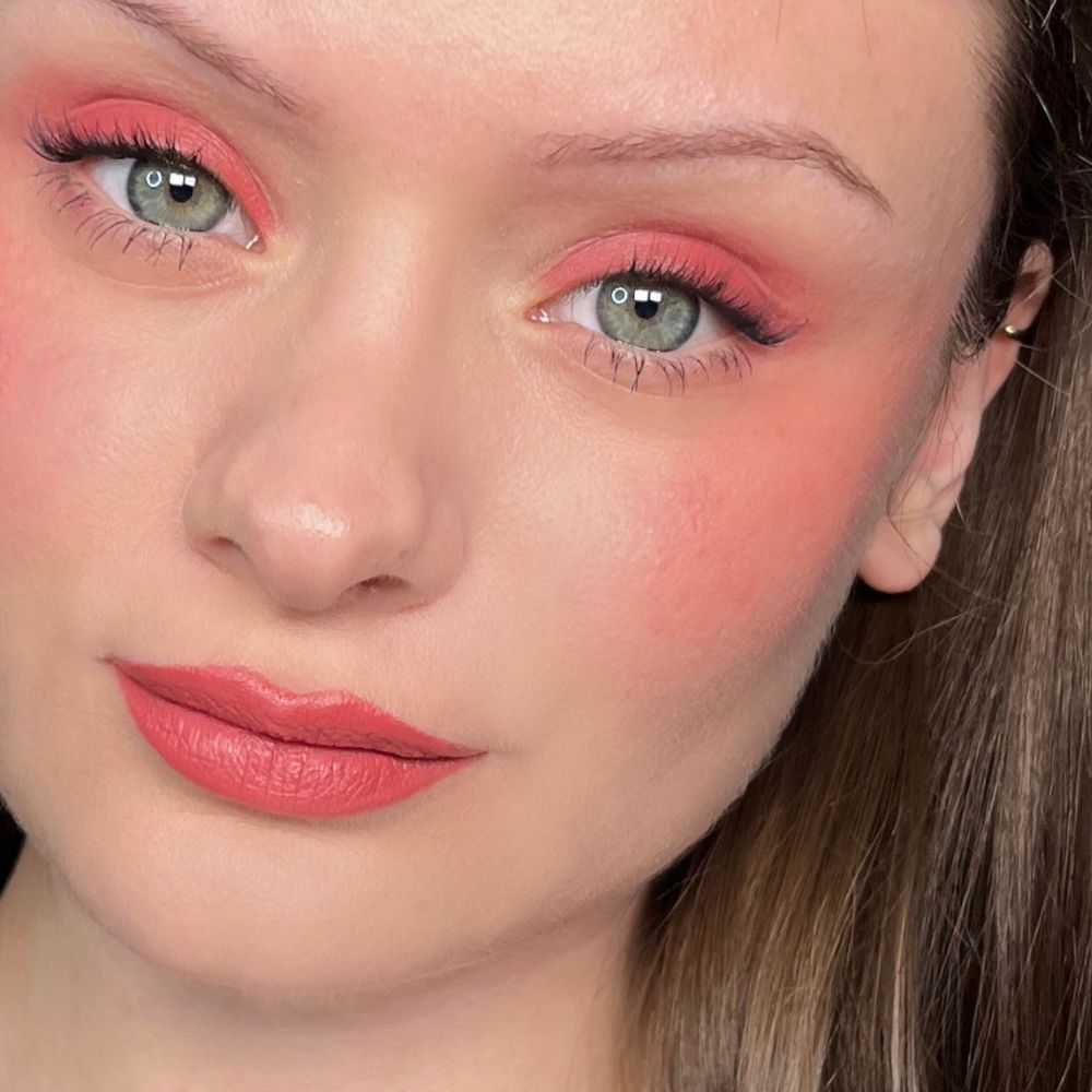 Close-up van een gezicht met make-up. Roze oogschaduw, blush en lippenstift. Groene ogen.