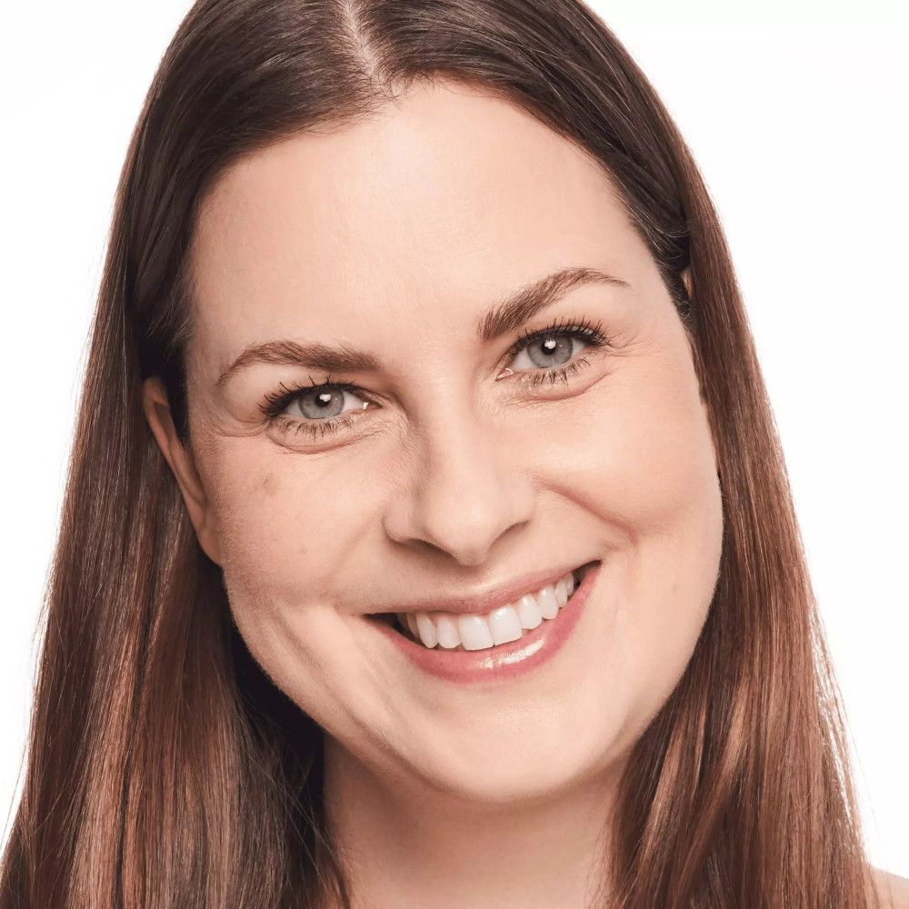 Portrait d'une femme aux cheveux bruns. Elle sourit. Fond clair.