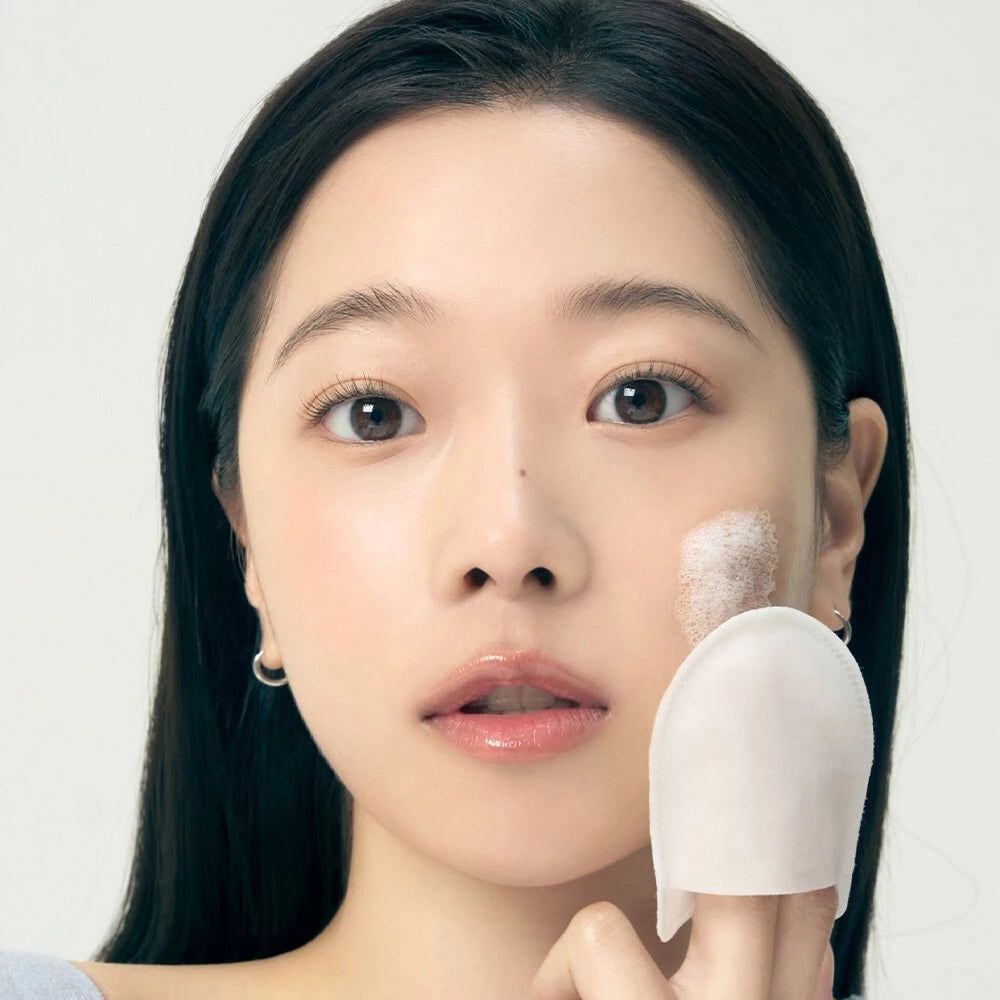 Person utilisant un pad. Mousse sur la peau. Pad en tissu blanc, doigts touchant le pad. Fond clair.