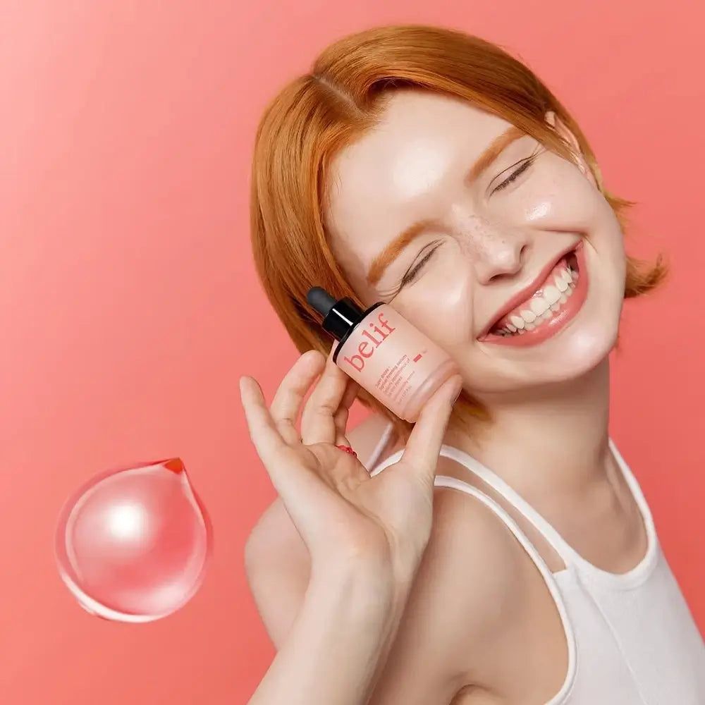 Vrouw met rood haar houdt Belif Super Drops serum vast. Bel op de voorgrond.