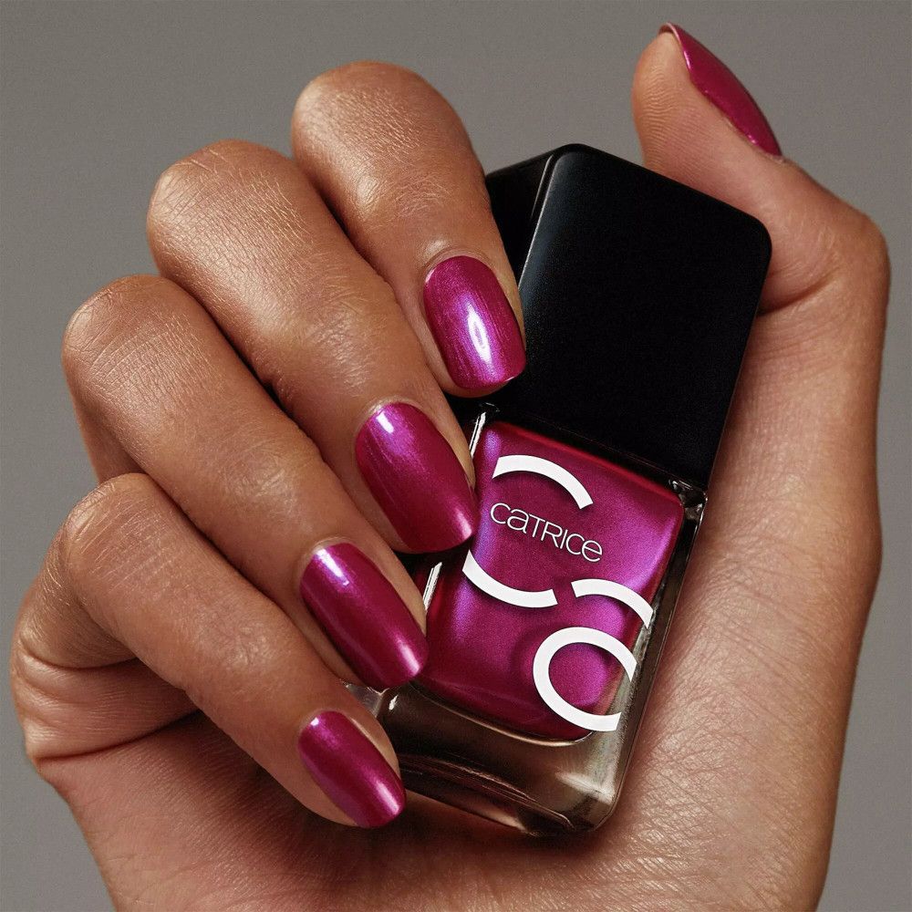 Main avec ongles vernis et flacon de vernis à ongles. Ongles violets, flacon avec bouchon noir, marque Catrice.
