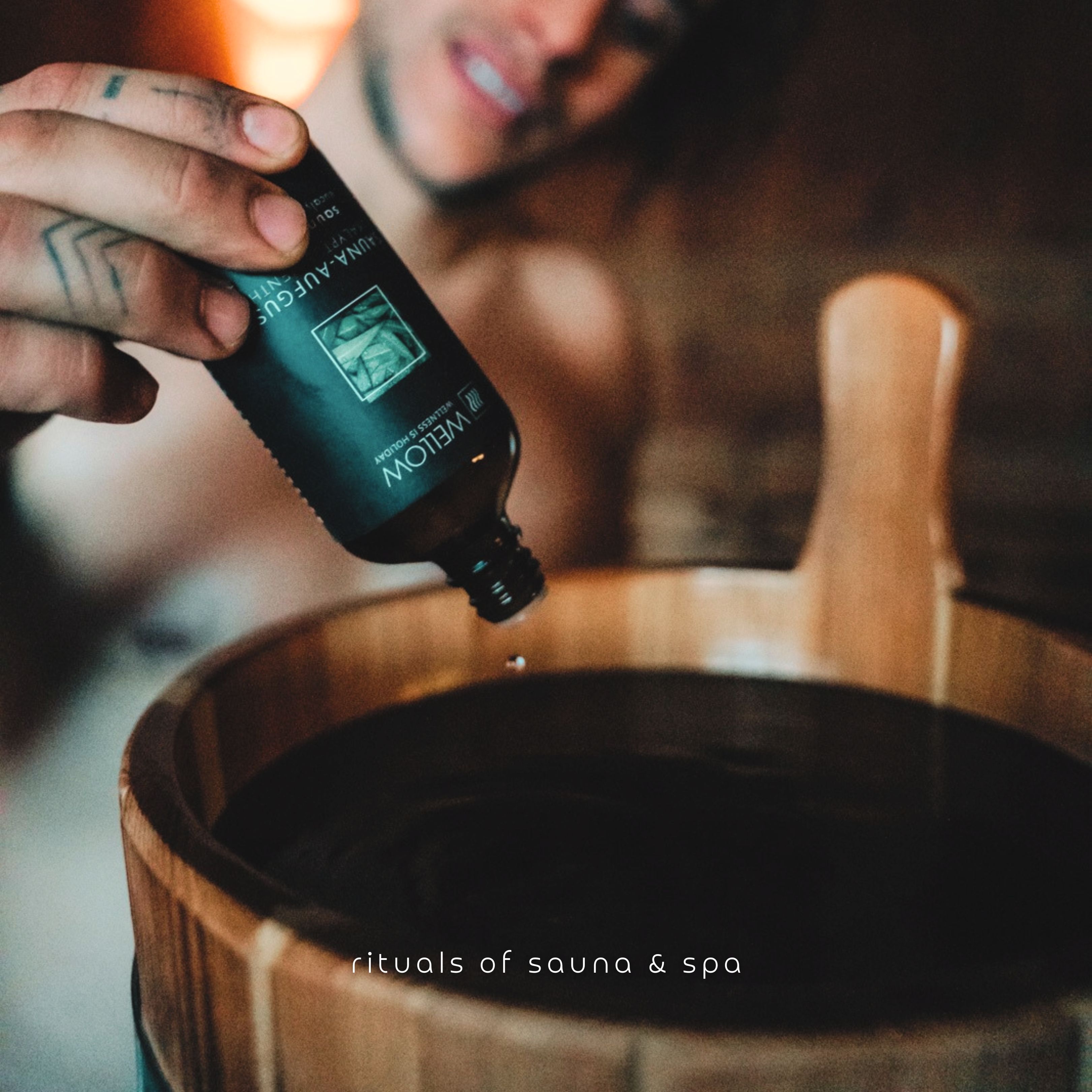 Man giet vloeistof uit een fles in een houten emmer. Opschrift op de fles: Sauna-Aufguss.