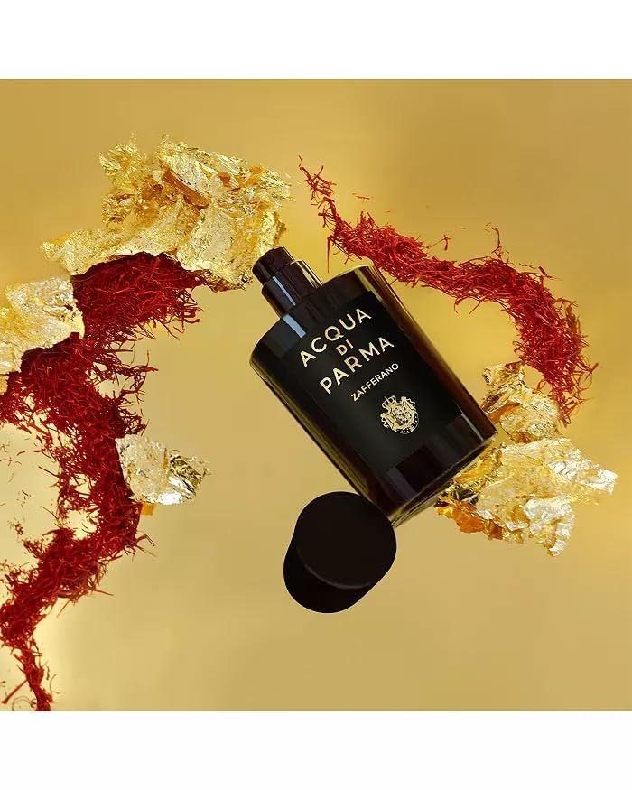 Zwarte flacon met opschrift ACQUA DI PARMA Zafferano. Open dop ernaast. Op gouden achtergrond met saffraan en bladgoud.