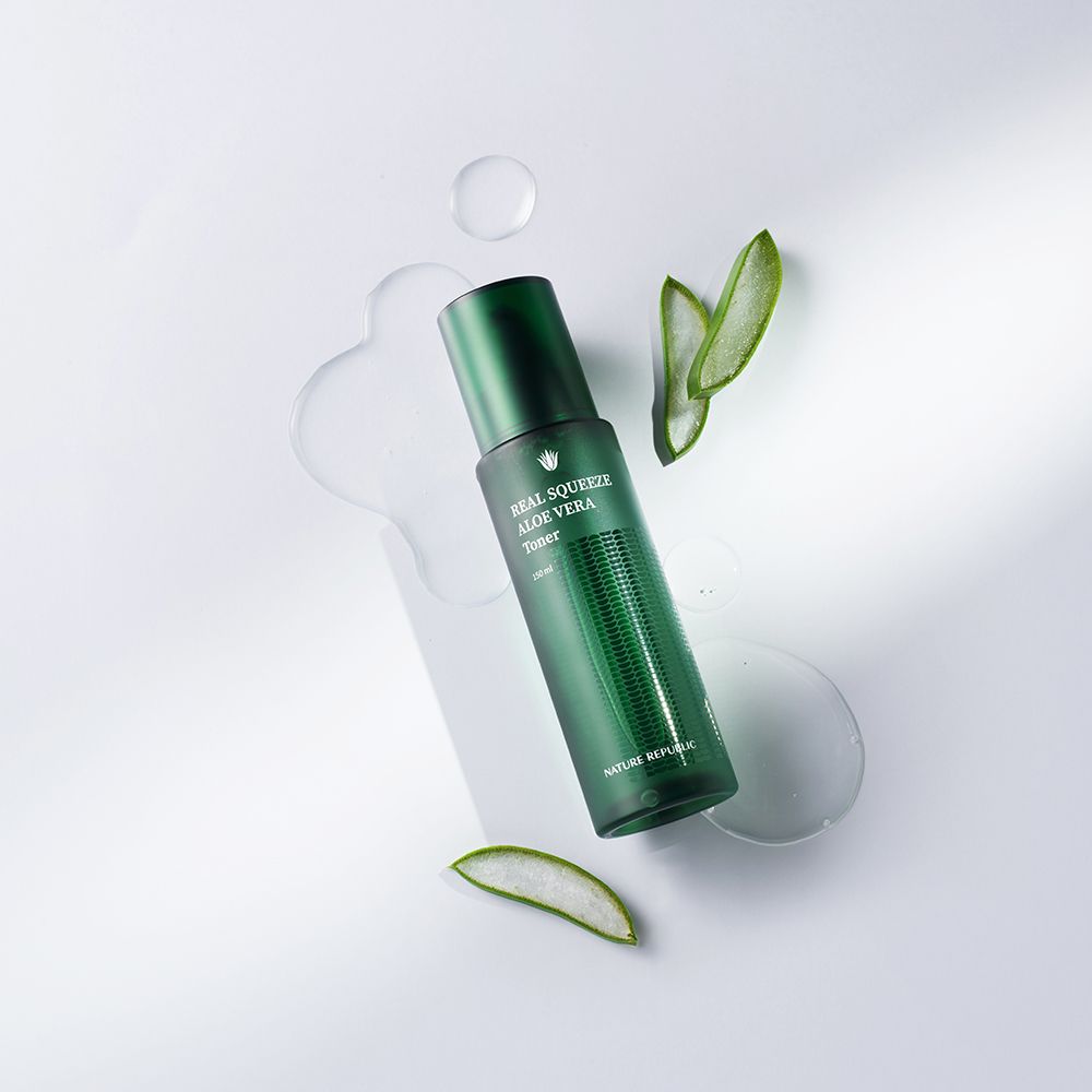 Flacon vert de toner à l'aloe vera, entouré de feuilles et liquide sur fond blanc.