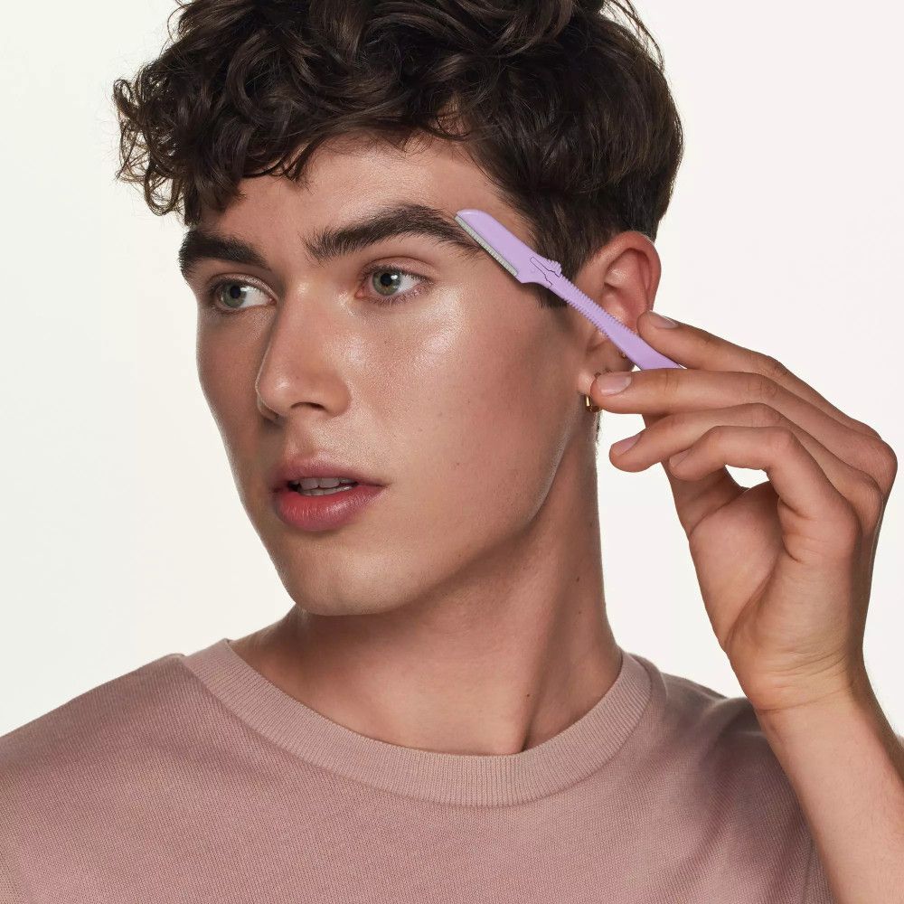 Personne tenant un formateur de sourcils lilas clair. Visage de profil. Le formateur est appliqué sur le sourcil.