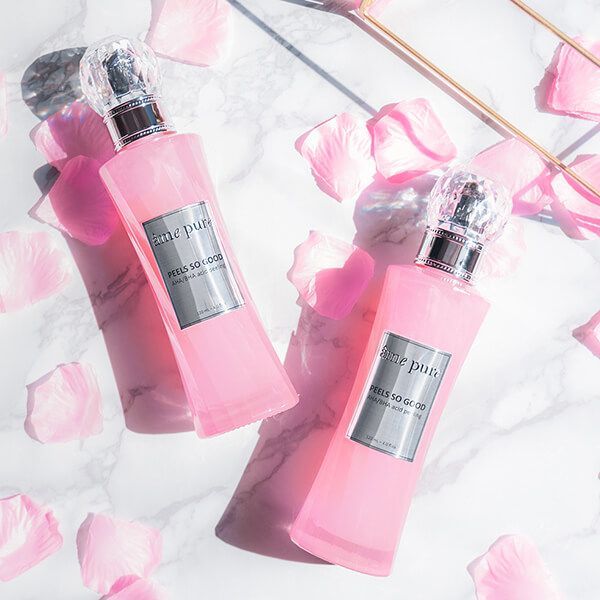 Twee roze flacons van de "Peels So Good" peeling van âme pure op marmeren ondergrond met rozenblaadjes.