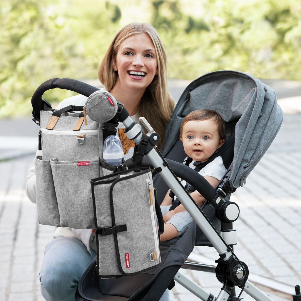 Vrouw met baby in kinderwagen, tas bevestigd. Fles en aankleedkussen zichtbaar.