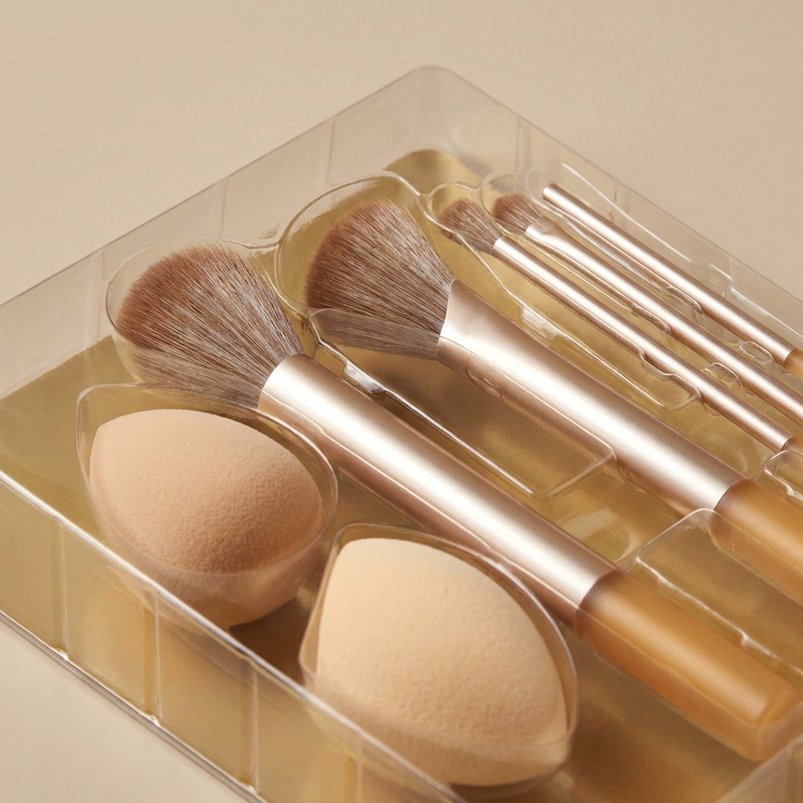Ensemble de pinceaux et éponges de maquillage dans un emballage transparent. Poignées dorées, poils bruns.