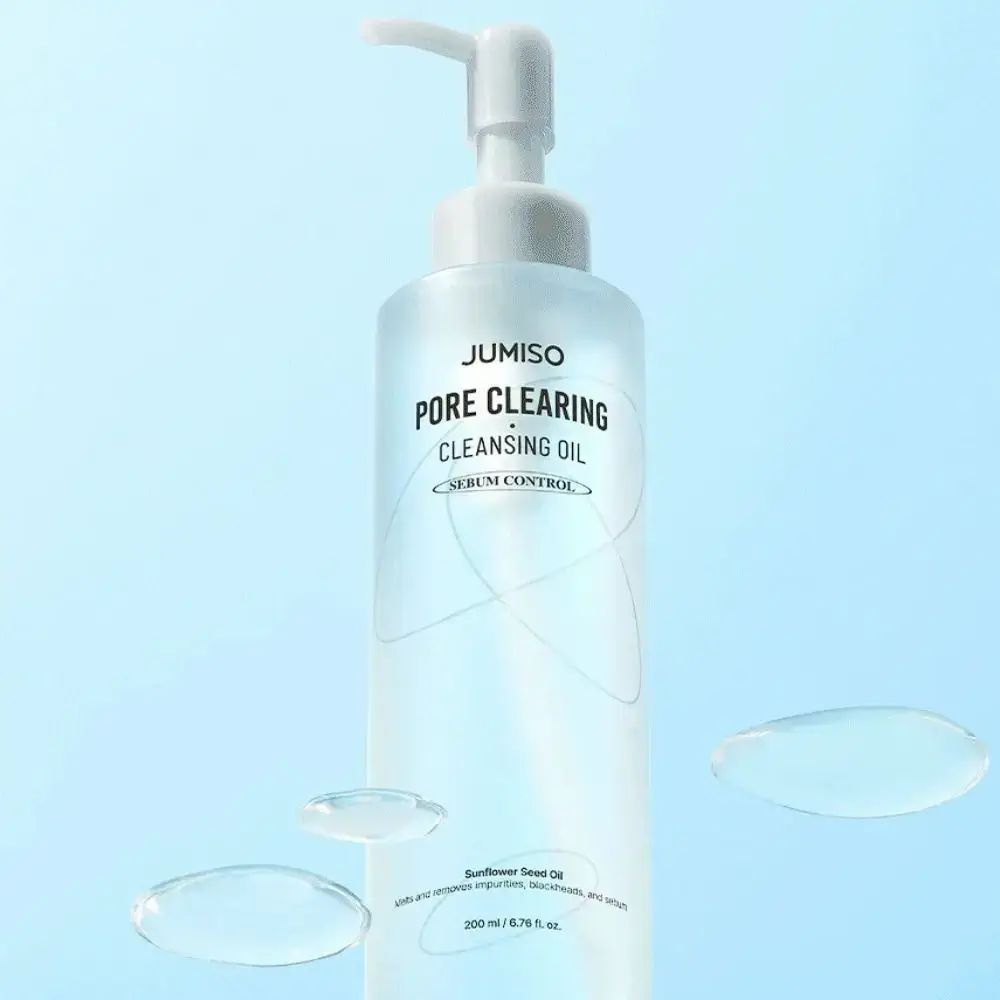 Transparante fles met pomp. Opschrift: JUMISO PORE CLEARING CLEANSING OIL. Serum Control. Waterdruppels op de achtergrond.