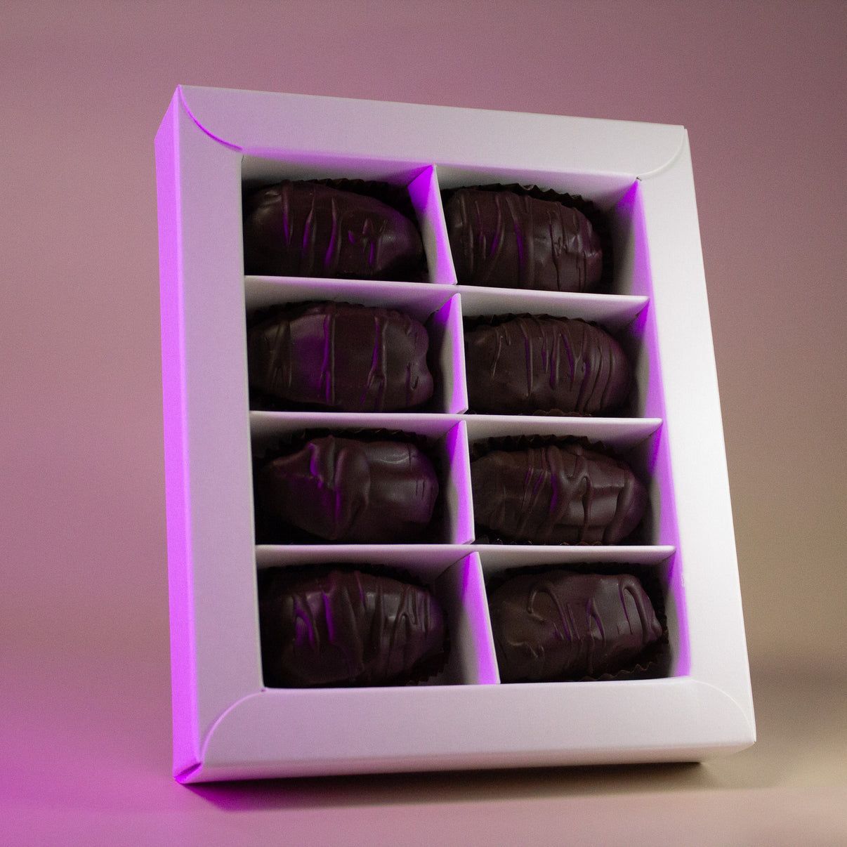 Six dattes enrobées de chocolat noir dans une boîte cadeau blanche.