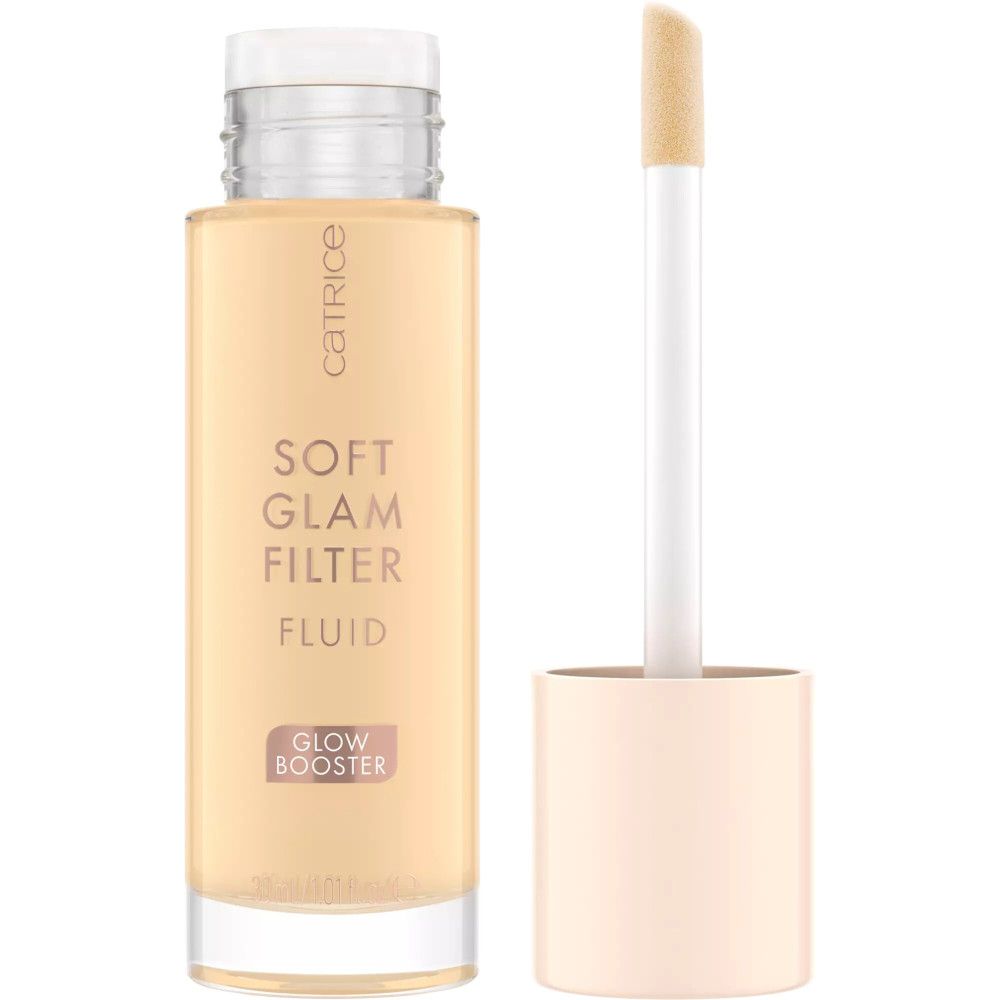 Flacon transparent avec bouchon blanc et applicateur. Inscription : Catrice, Soft Glam Filter Fluid, Glow Booster.