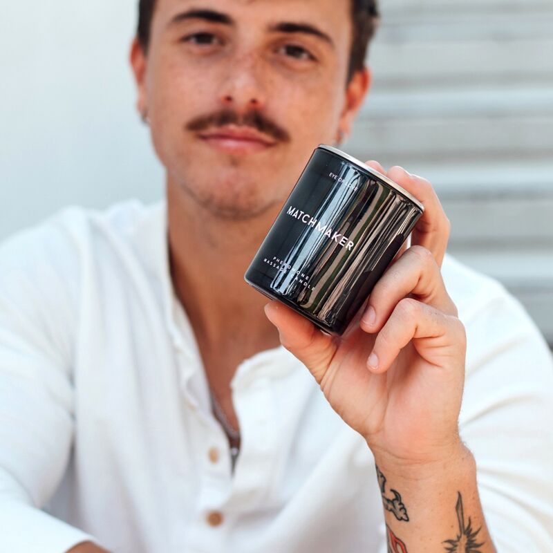 Un homme tenant une bougie de massage noire 'Matchmaker' par Eye of Love.
