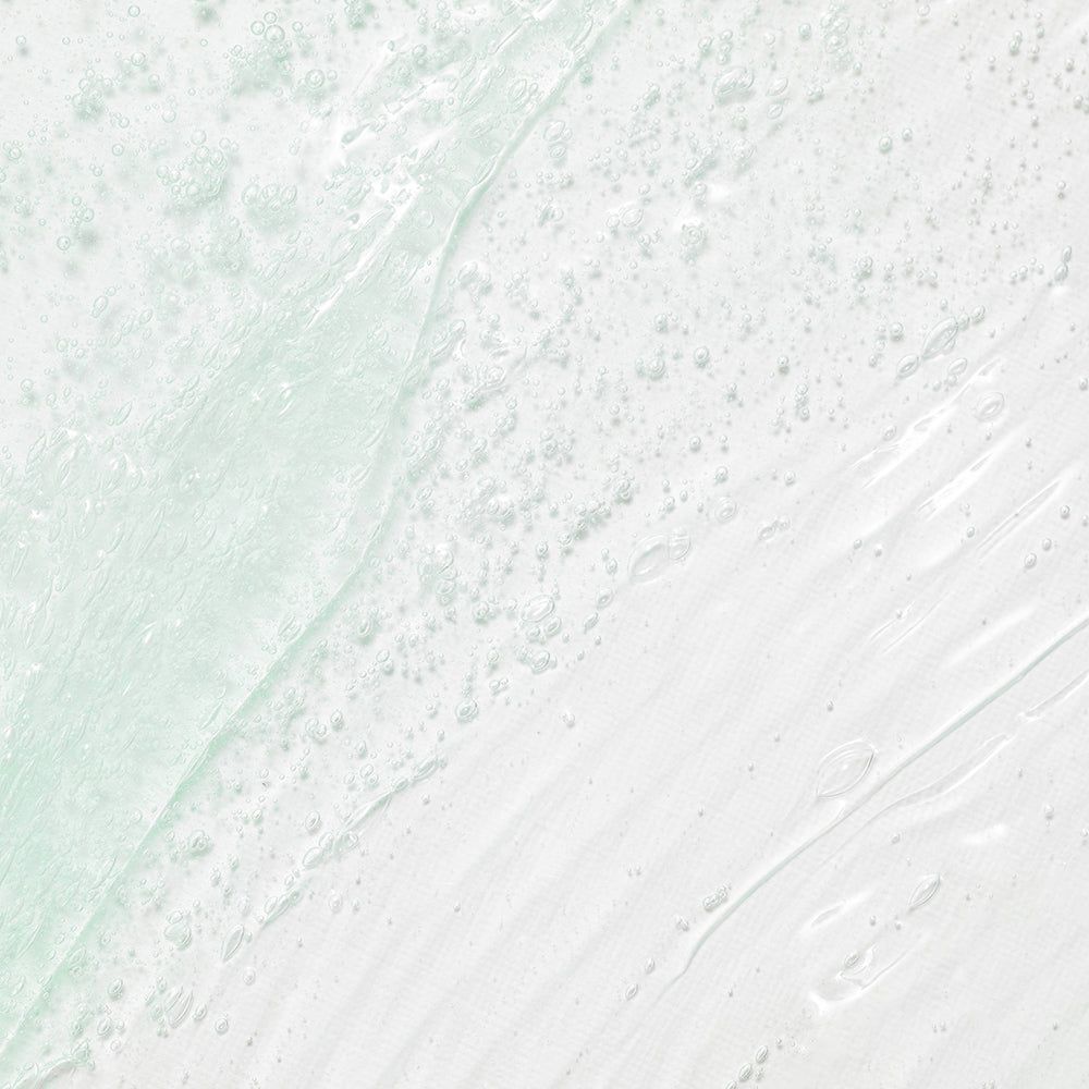 Une texture gel transparente vert pâle avec de petites bulles d'air, étalée sur une surface blanche.