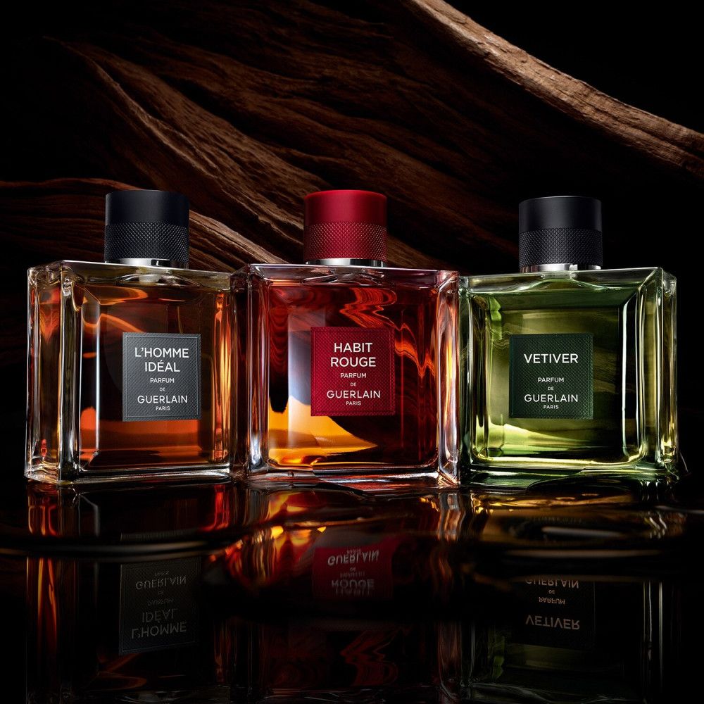 Trois flacons en verre. Gauche : "L'HOMME IDEAL". Centre : "HABIT ROUGE". Droite : "VETIVER". Tous "GUERLAIN PARIS".