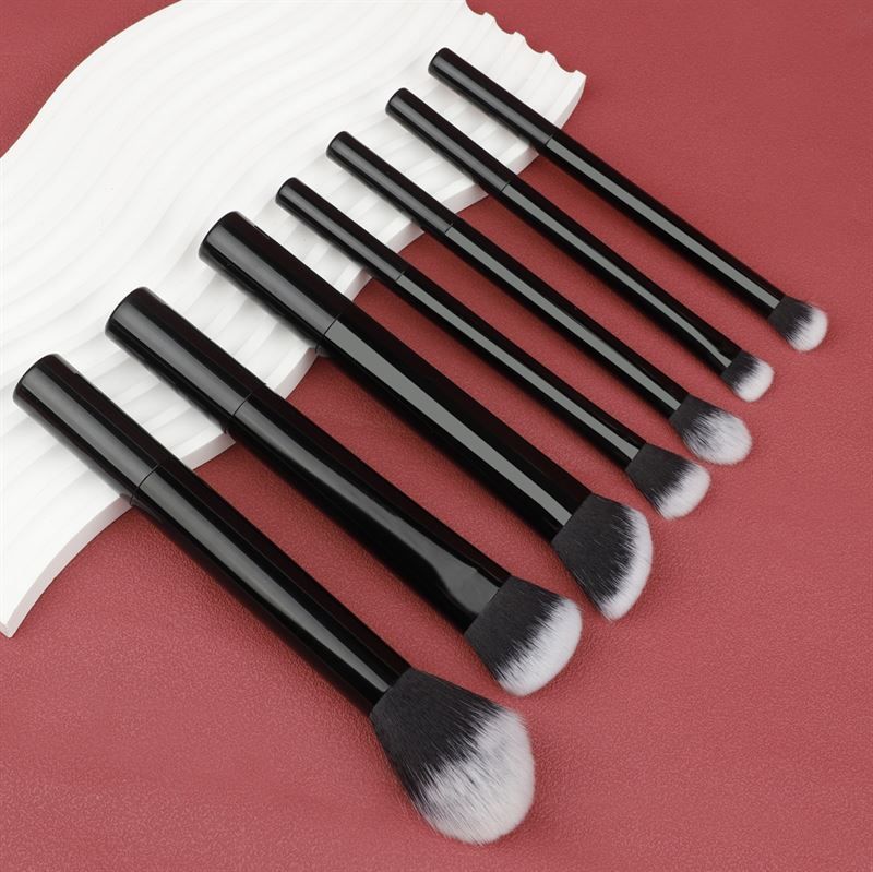 Sept pinceaux de maquillage noirs avec poils blancs, disposés sur fond rouge. Différentes formes.