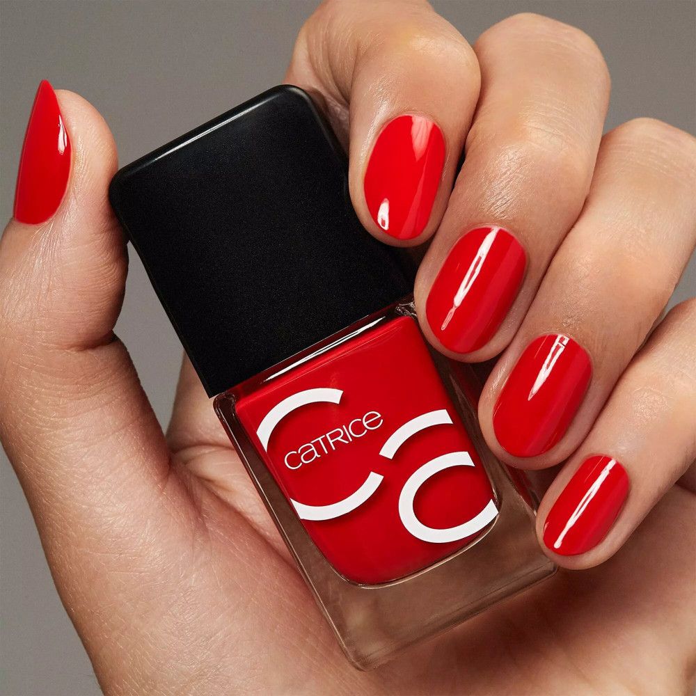 Main avec ongles rouges vernis et flacon de vernis à ongles. Catrice est écrit sur le flacon.