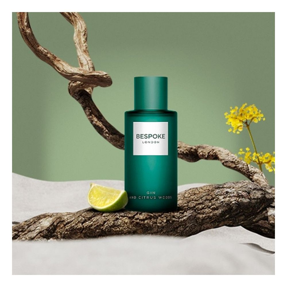 Flacon vert avec étiquette blanche, texte: Bespoke London, Gin and Citrus Woods. Tranche de citron vert et branches en arrière-plan.
