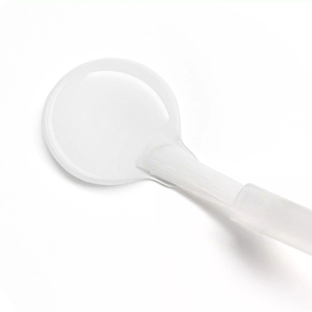 Liquide transparent sur une surface ronde avec un pinceau. Le pinceau est blanc et possède un manche transparent.