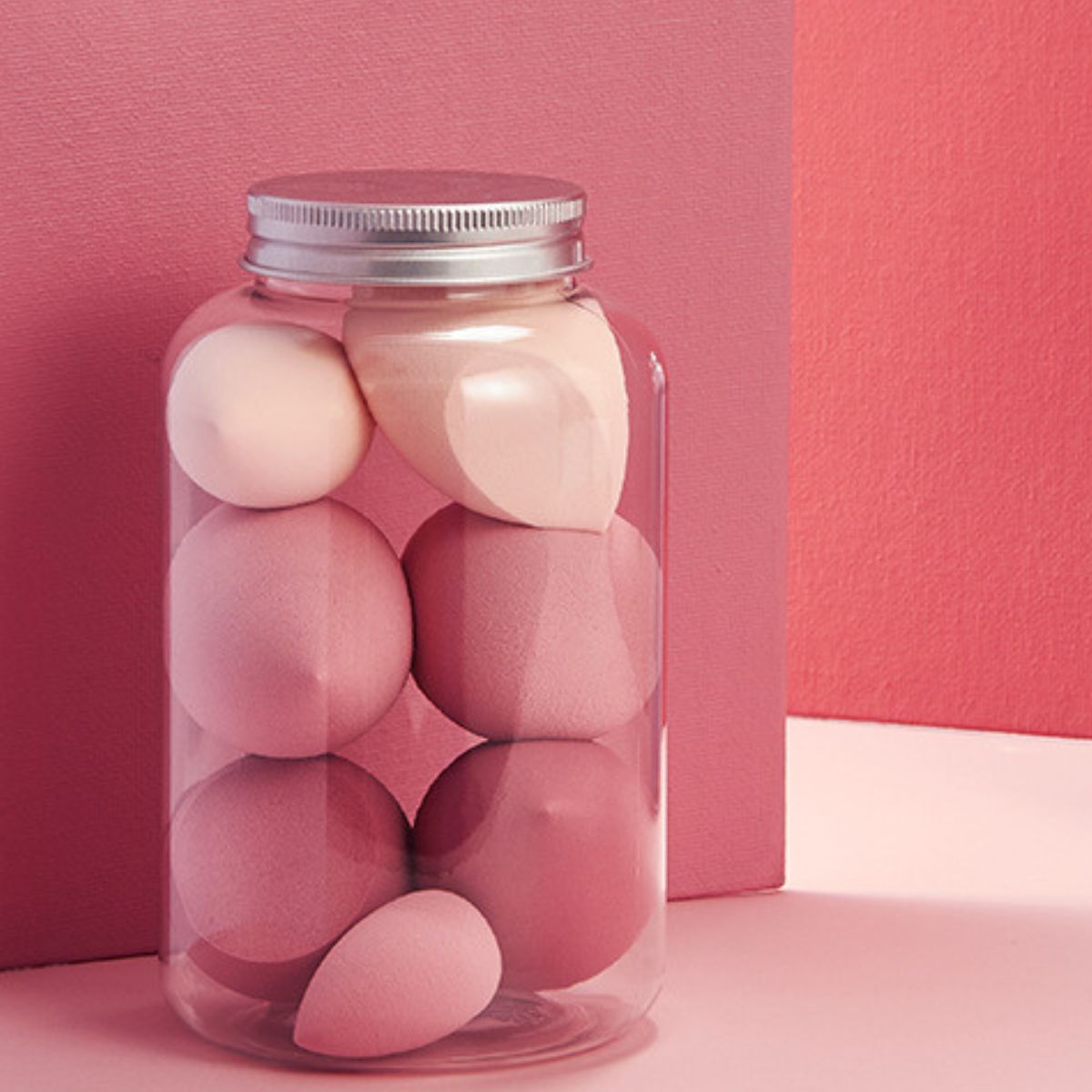 Roze make-upsponzen in een transparante pot met zilveren deksel. Verschillende roze vormen.