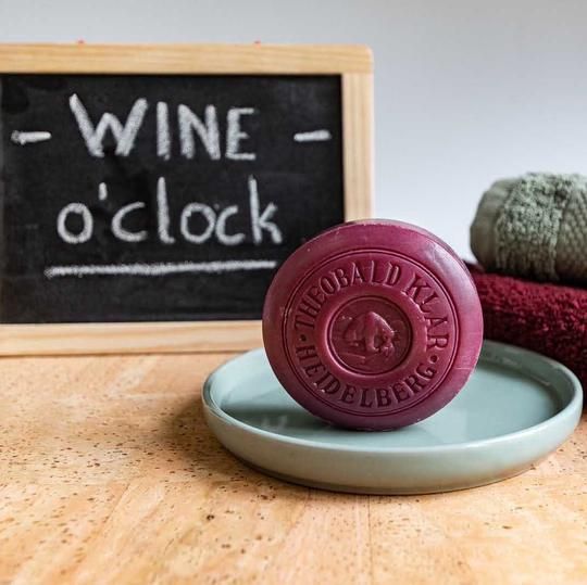 Ronde, bordeauxrode zeep op een bord. Op de achtergrond een bord met de tekst 'WINE o'clock'.