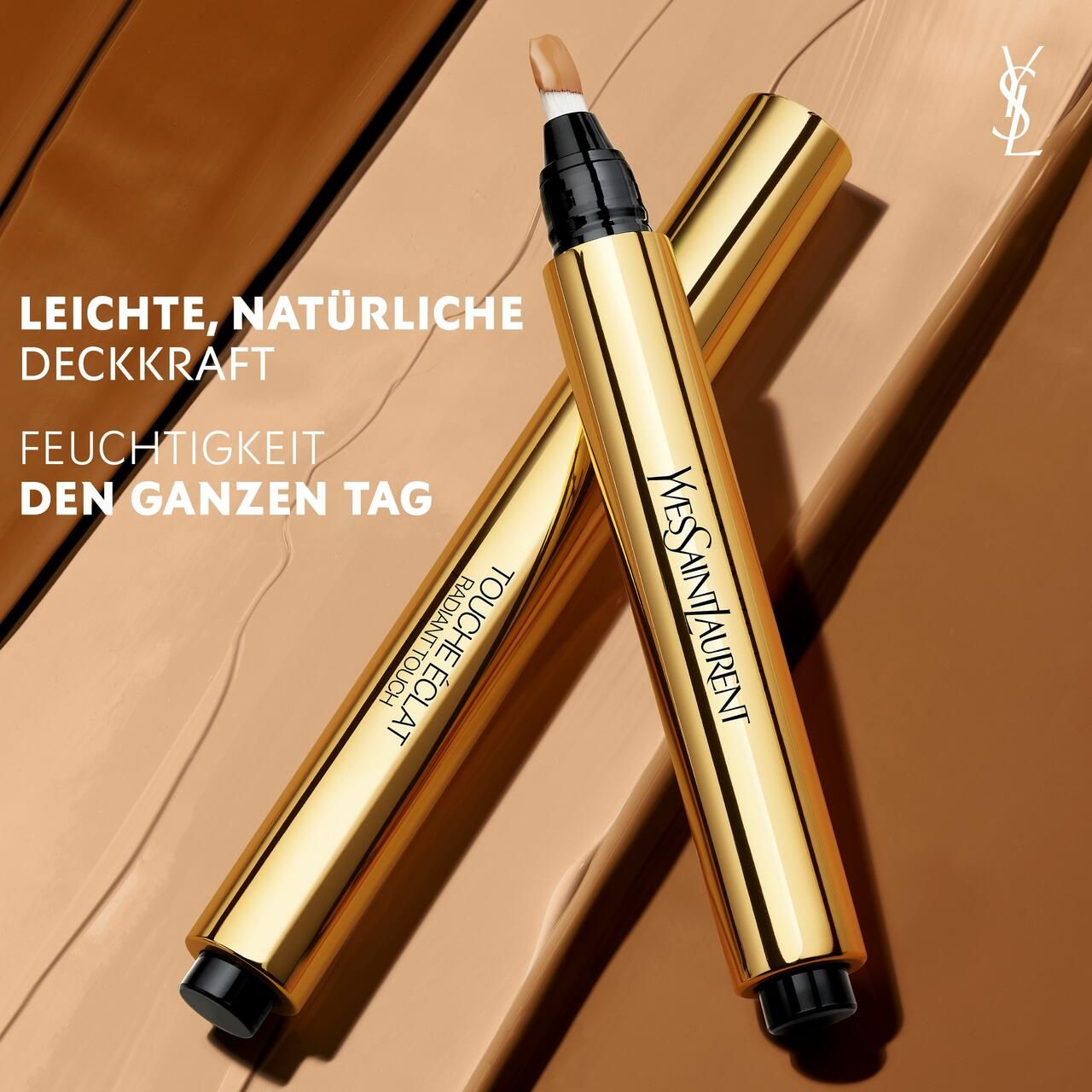 Twee gouden pennen. YSL Touche Éclat. Tekst op de pen. Op bruine achtergrond.