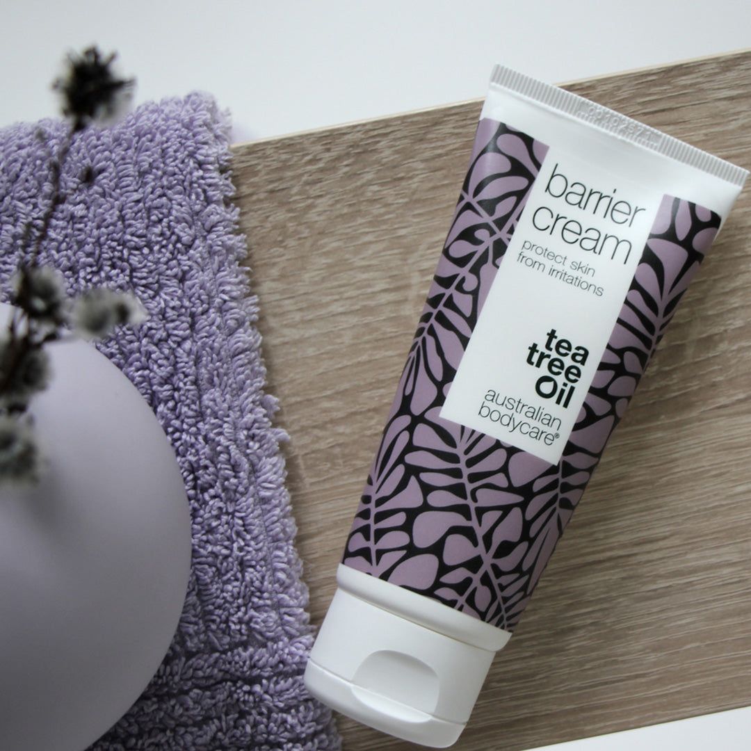 Tube Barrier Cream met bloemmotief, naast een paarse handdoek en vaas. Merk: Australian Bodycare.