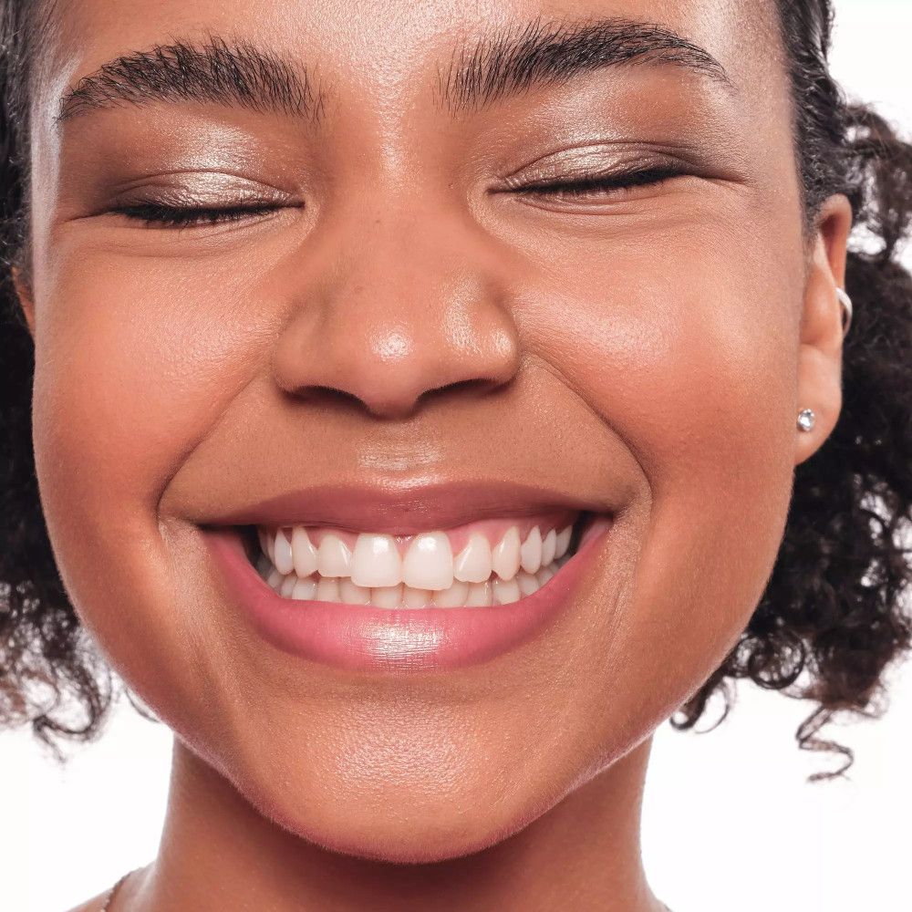 Gros plan sur un visage souriant. La femme porte du fard à paupières et du rouge à lèvres. Sur fond blanc.